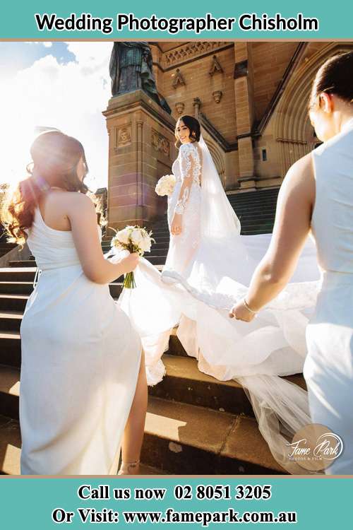 The Bride smiles as the bridesmaids holding the tail of her gown in front of the church Chisholm