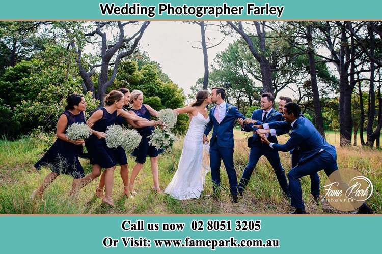 Photo of the Bride and the Groom kissing while teasing by their groom men and bridesmaids Farley NSW 2320