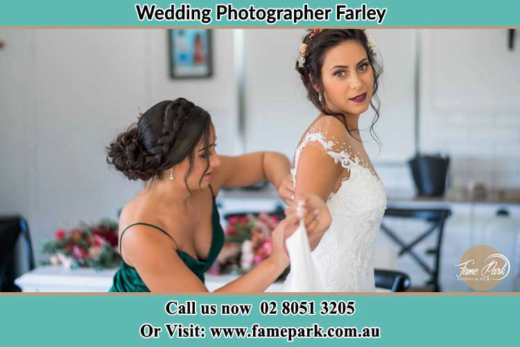 The Bride is being helped by bridesmaid trying to put her bridal gown Farley