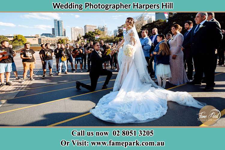 The Groom half kneeling before his Bride as the crowd watching Harpers Hill