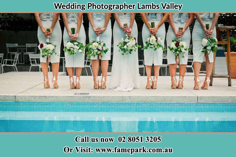 Photo of the Bride and her bridesmaids striking a pose of their behind holding a flower near the swimming pool Lambs Valley NSW 2335