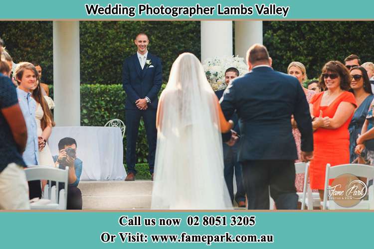 Behind photo of the Bride accompany by her father walking the aisle going to the waiting Groom Lambs Valley NSW 2335