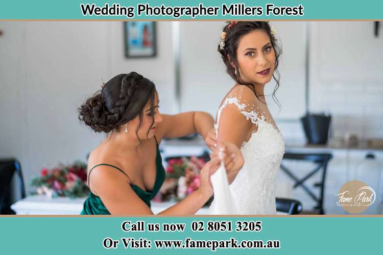 Photo of the Bride assisting by her bridesmaid fitting her wedding gown Millers Forest NSW 2324