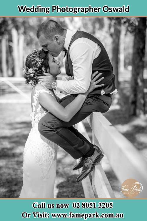 The Groom on the fence kissing her Bride at her forehead Oswald