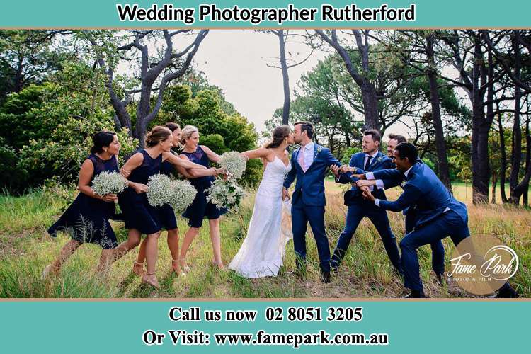 Photo of the Bride and the Groom kissing while teasing by their entourage Rutherford NSW 2320