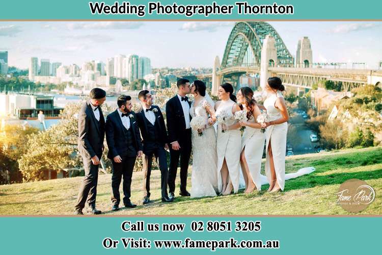 Photo of the Groom and the Bride kissing near the bridge while being watched by their entourage Thornton